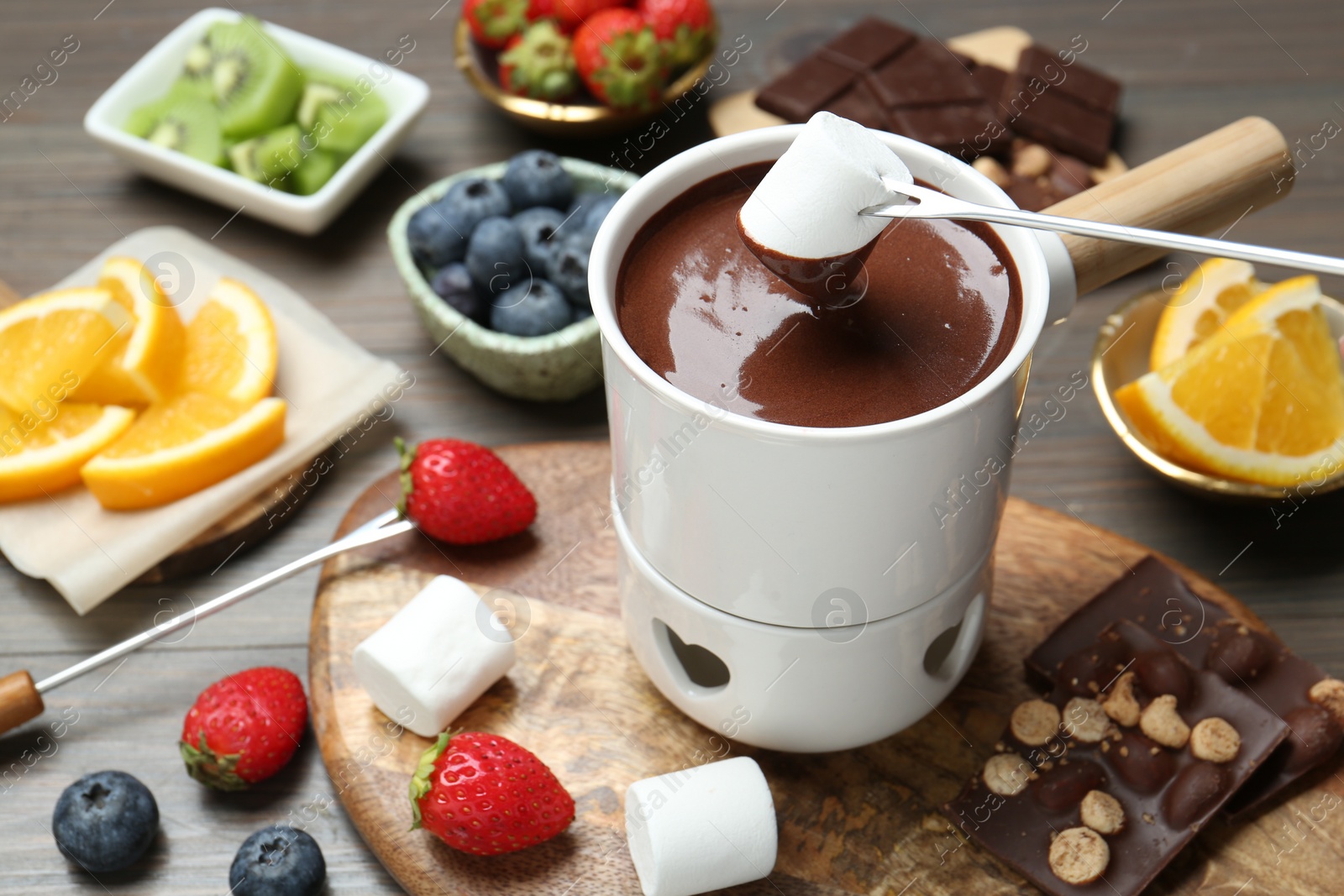 Photo of Dipping sweet marshmallow in fondue pot with melted chocolate at wooden table