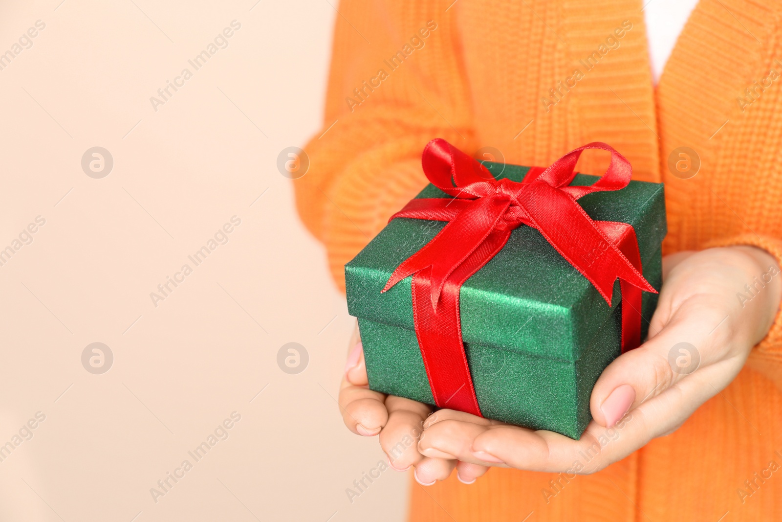 Photo of Woman holding beautifully wrapped Christmas gift box on beige background, closeup. Space for text