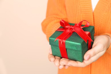Photo of Woman holding beautifully wrapped Christmas gift box on beige background, closeup. Space for text