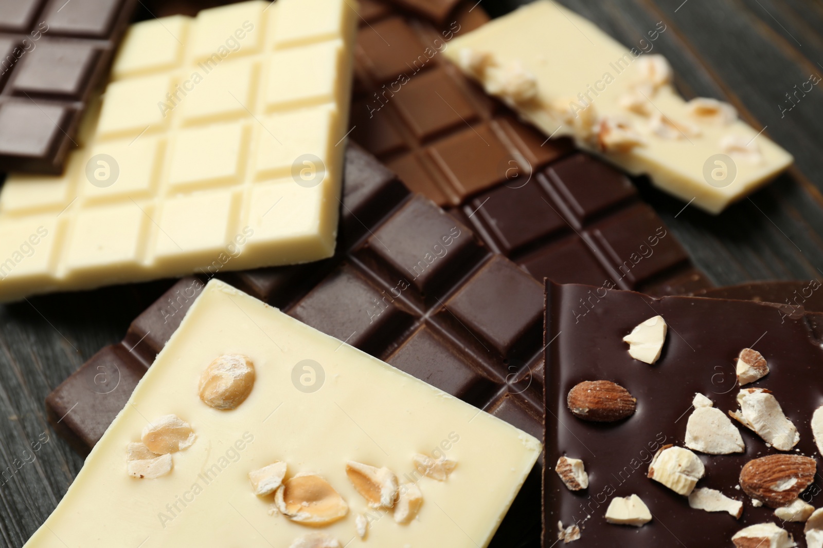 Photo of Different chocolate bars with nuts on wooden background, closeup