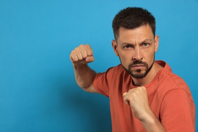 Man ready to fight on light blue background, space for text