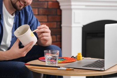 Photo of Man learning to decorate cup while watching online course at home, closeup. Time for hobby