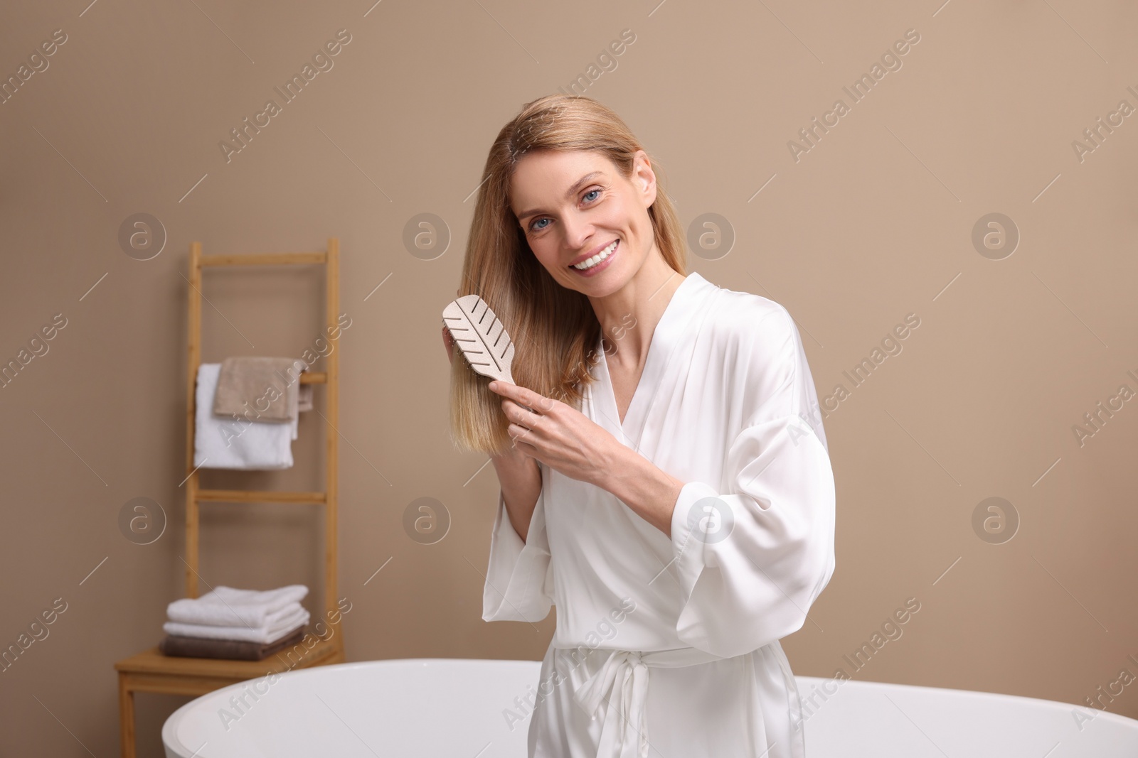 Photo of Beautiful woman brushing her hair near tub in bathroom