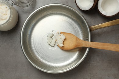 Photo of Frying pan with coconut oil and wooden spatula on grey table, flat lay. Healthy cooking