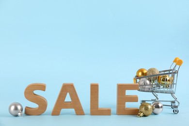 Photo of Word Sale made with wooden letters and Christmas decor in shopping cart on light blue background