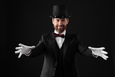 Happy magician in top hat on black background