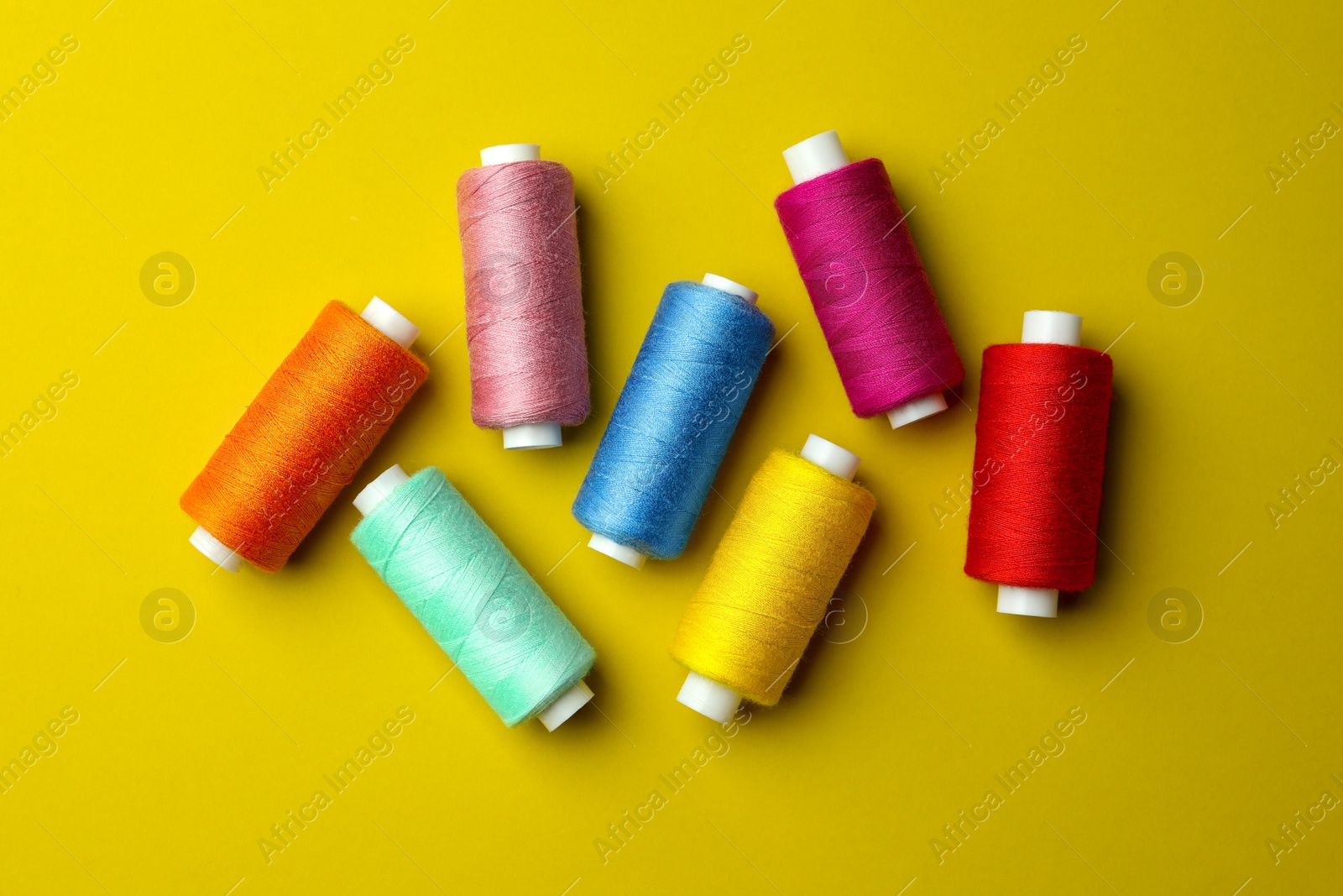 Photo of Different colorful sewing threads on yellow background, flat lay