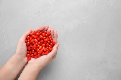 Woman holding fresh goji berries on grey background, top view. Space for text