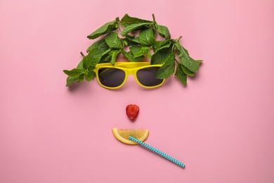 Photo of Funny face made of sunglasses, mint, strawberry, cocktail straw and citrus slice on color background, flat lay