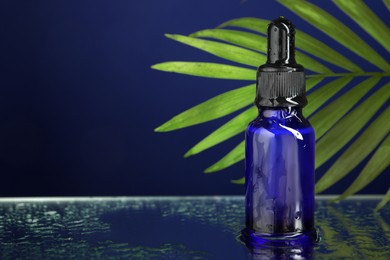 Photo of Bottle of face serum on wet surface against blue background, closeup. Space for text