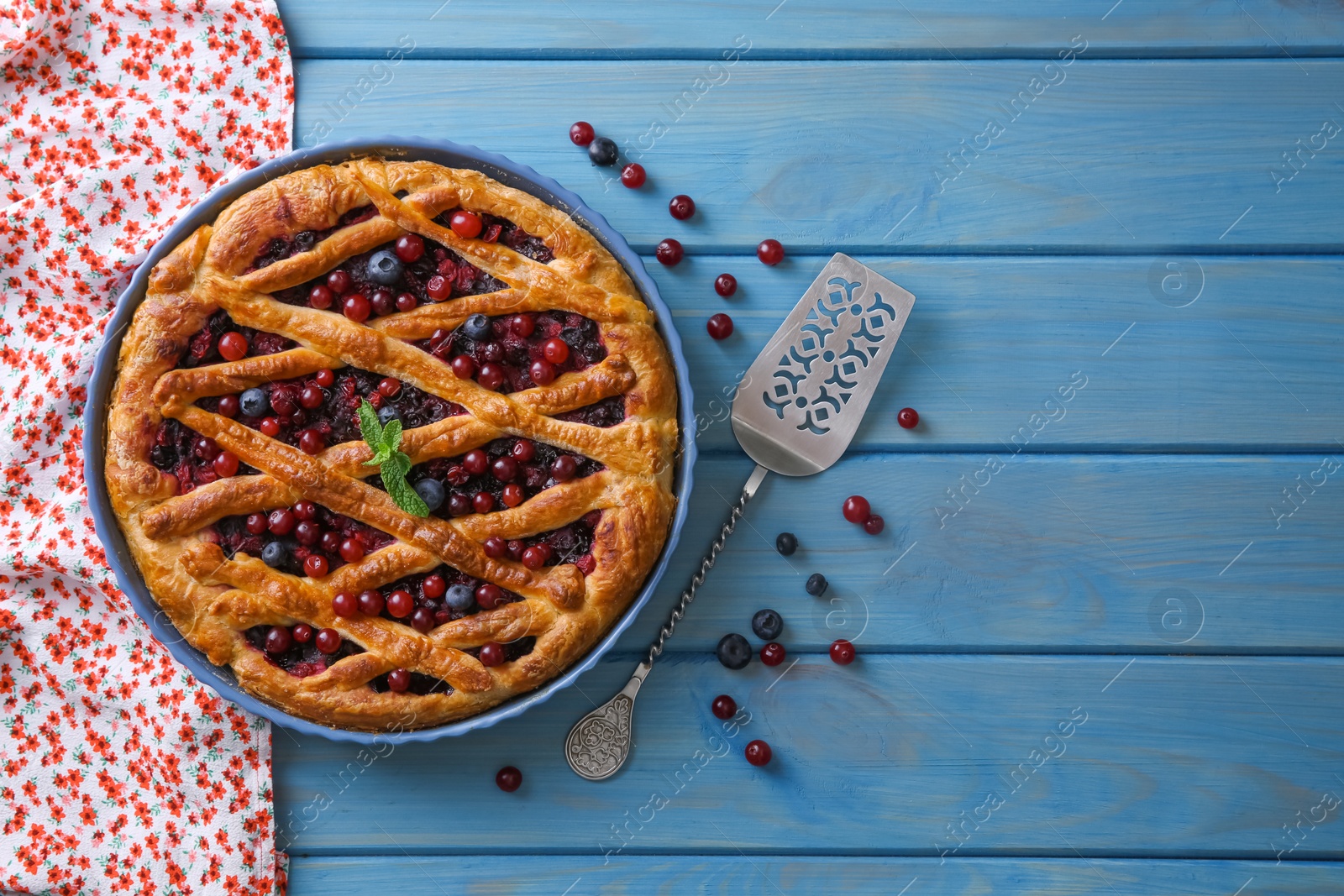 Photo of Delicious currant pie with fresh berries and spatula on blue wooden table, flat lay. Space for text