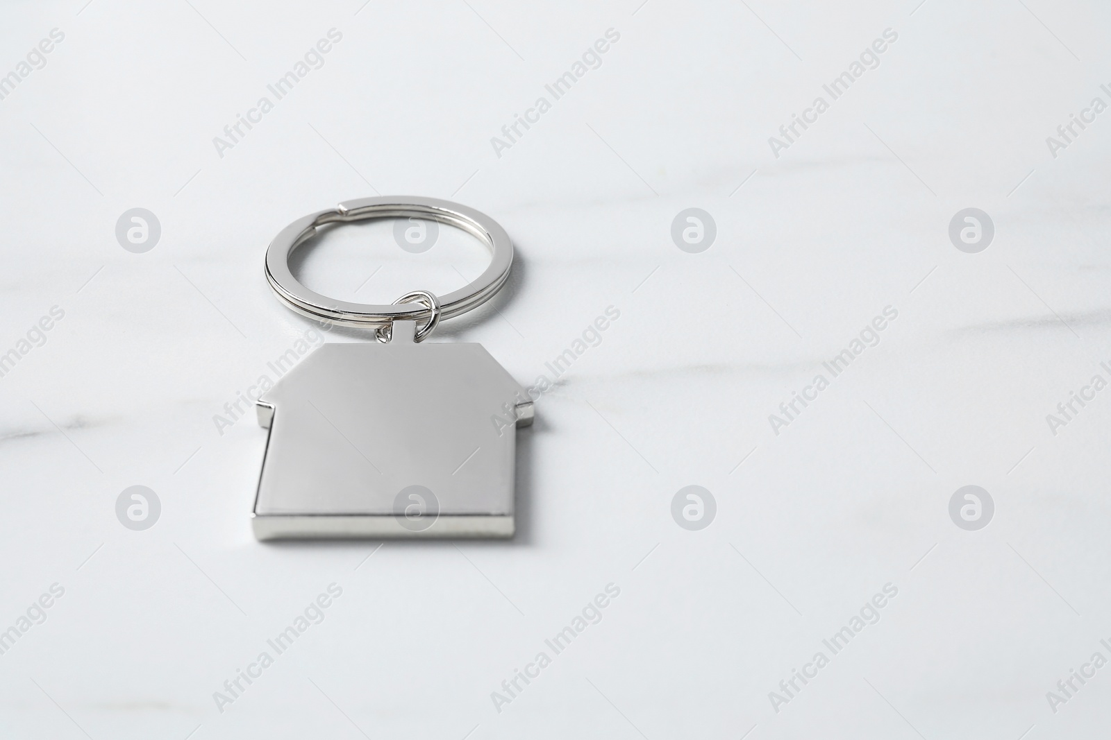 Photo of Metal keychain in shape of house on light marble table. Space for text