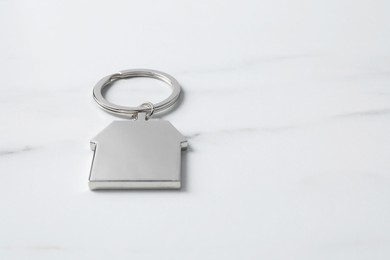 Metal keychain in shape of house on light marble table. Space for text