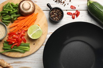 Flat lay composition with black wok and products on light wooden table