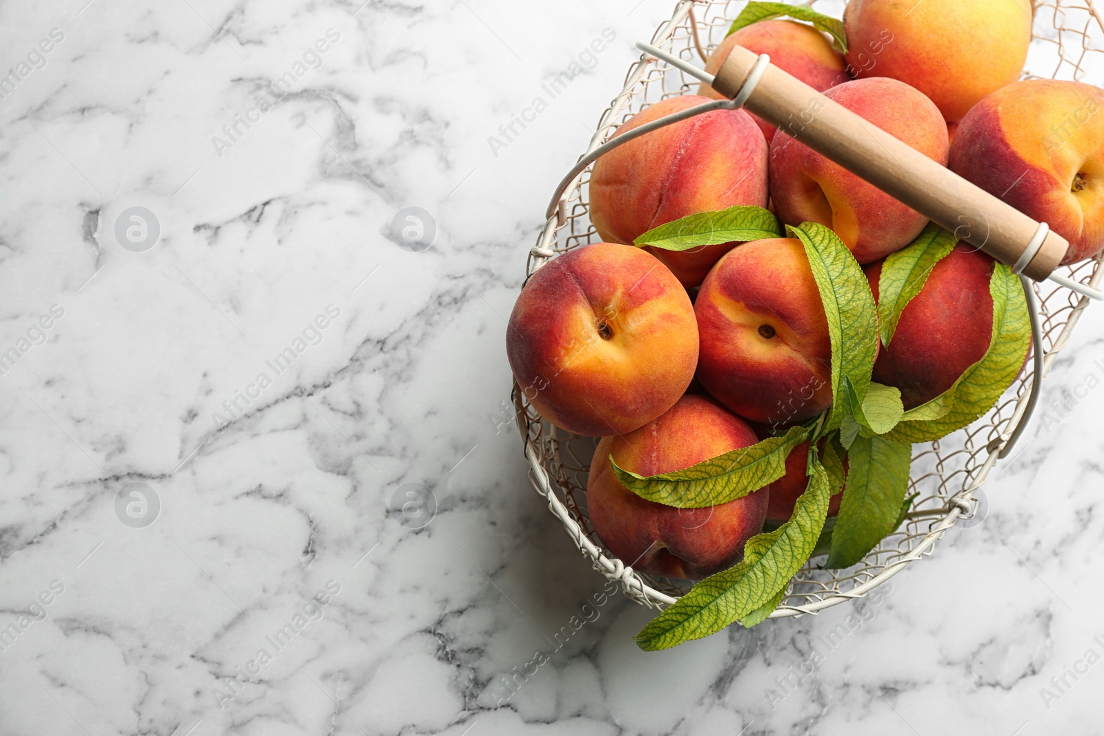 Photo of Fresh sweet peaches in metal basket on white marble table, top view. Space for text