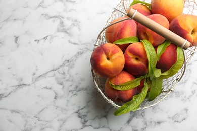 Photo of Fresh sweet peaches in metal basket on white marble table, top view. Space for text