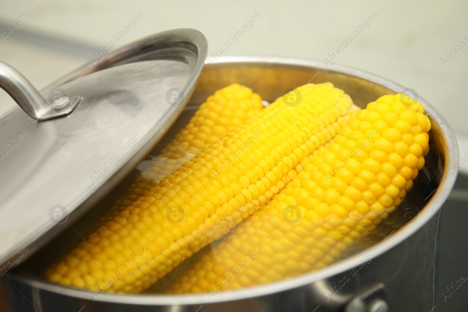 Photo of Pot with boiling corn cobs in kitchen, closeup