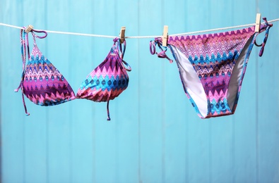 Photo of Stylish bikini hanging on rope against color background