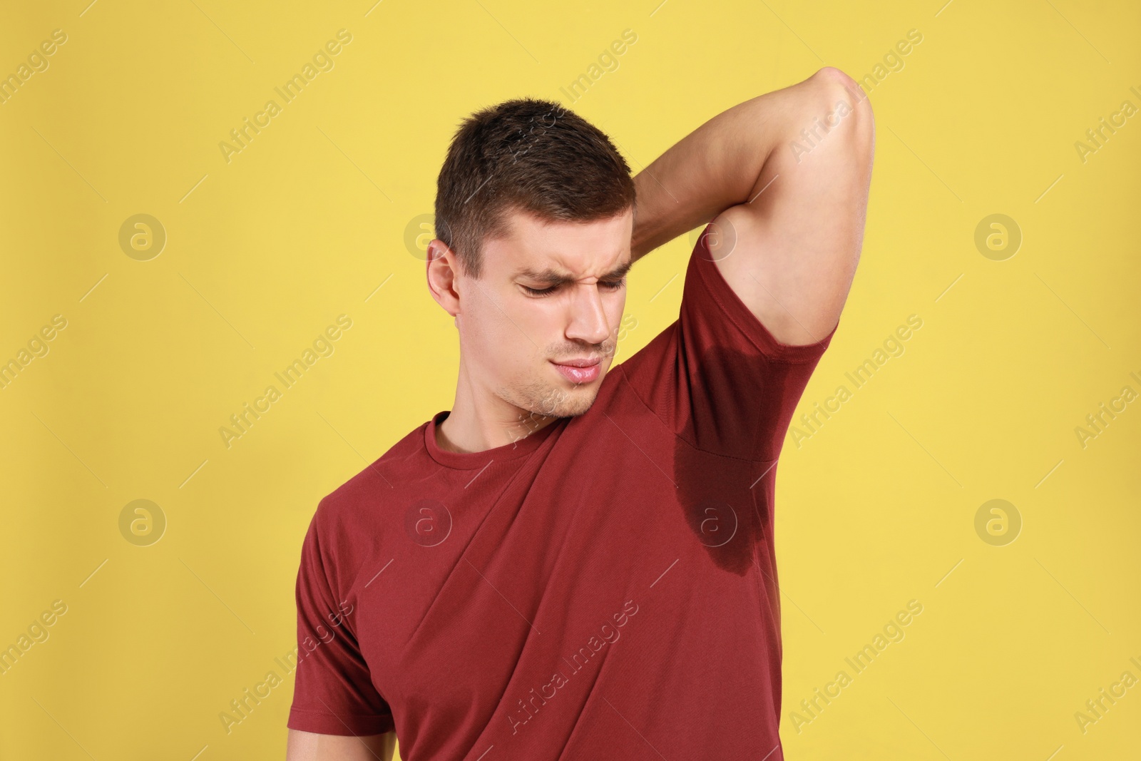 Photo of Young man with sweat stain on his clothes against yellow background. Using deodorant