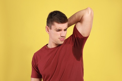 Young man with sweat stain on his clothes against yellow background. Using deodorant
