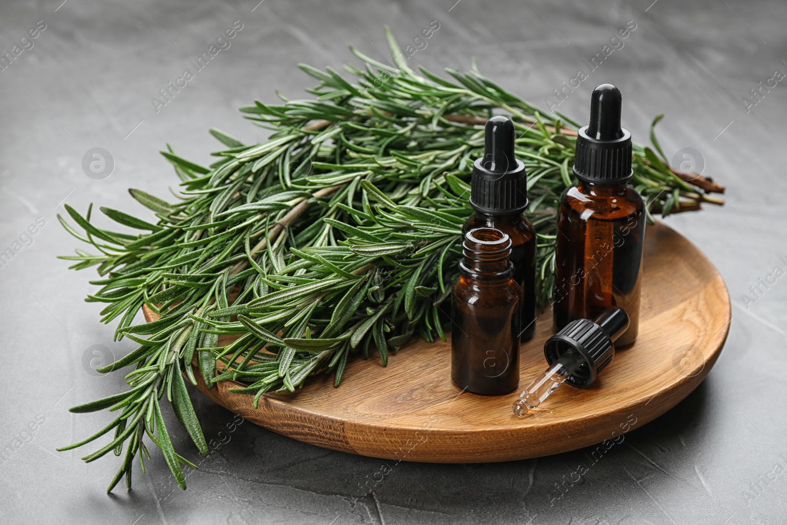 Photo of Fresh rosemary and bottles of essential oil on grey table