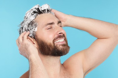 Photo of Happy man washing his hair with shampoo on light blue background, closeup