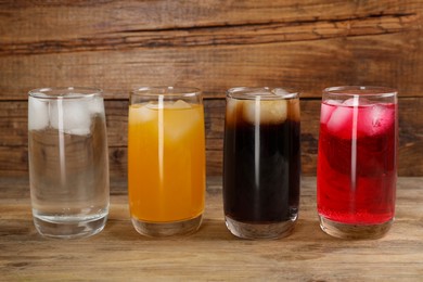 Glasses of different refreshing soda water with ice cubes on wooden table