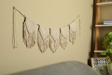 Photo of Beautiful large macrame hanging on beige wall in living room. Decorative element