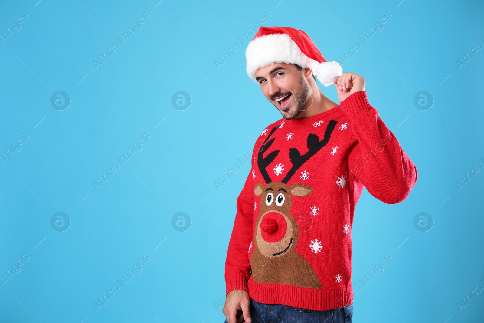 Photo of Portrait of young man in Christmas sweater and Santa hat on light blue background. Space for text