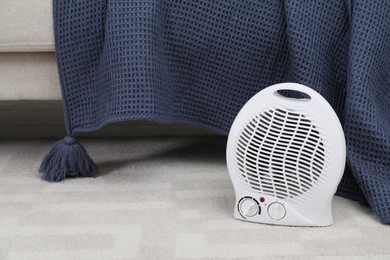 Photo of Portable electric fan heater on floor near sofa indoors