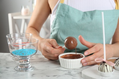 Photo of Young woman with cake pop in chocolate frosting at white marble table, closeup