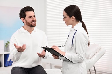 Doctor with clipboard consulting patient during appointment in clinic