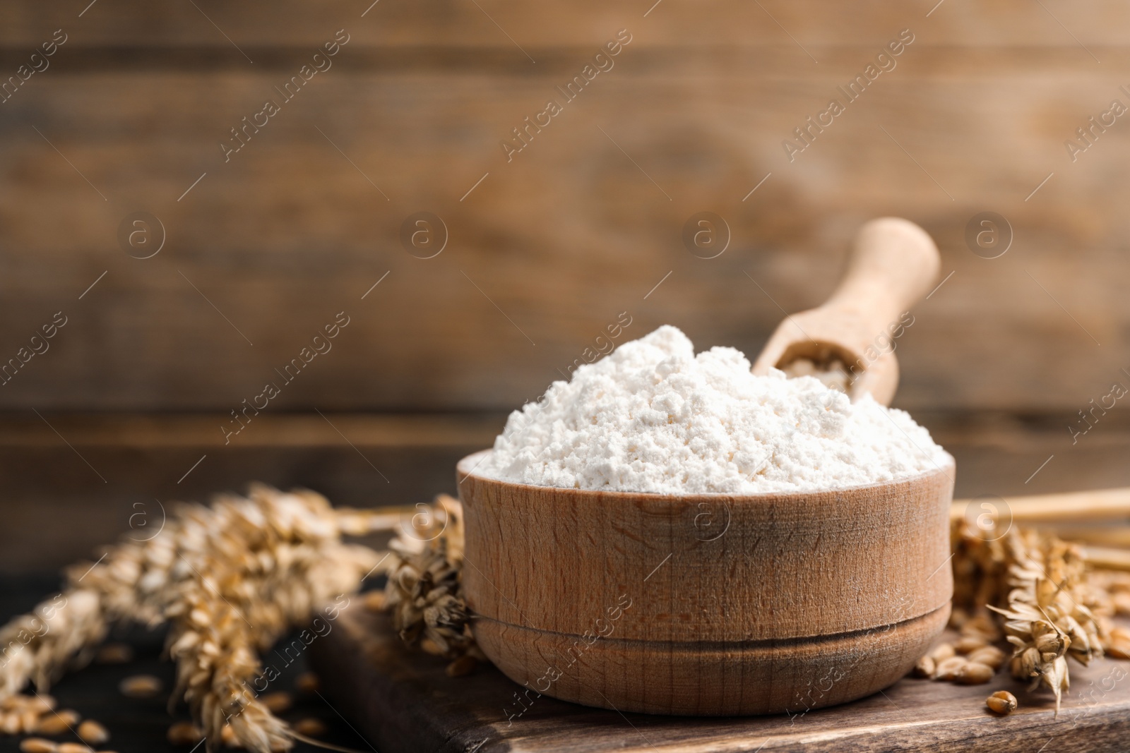 Photo of Wheat flour in bowl, spikes and grains on wooden board, closeup. Space for text