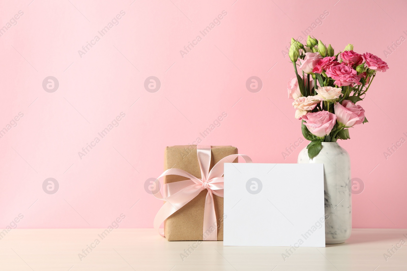 Photo of Happy Mother's Day. Gift box, blank card and bouquet of beautiful flowers in vase on white table against pink background. Space for text