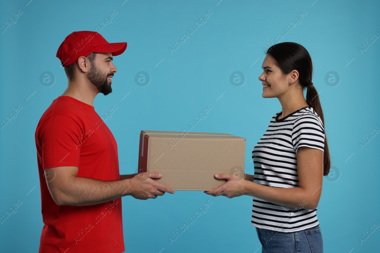 Photo of Smiling courier giving parcel to receiver on light blue background