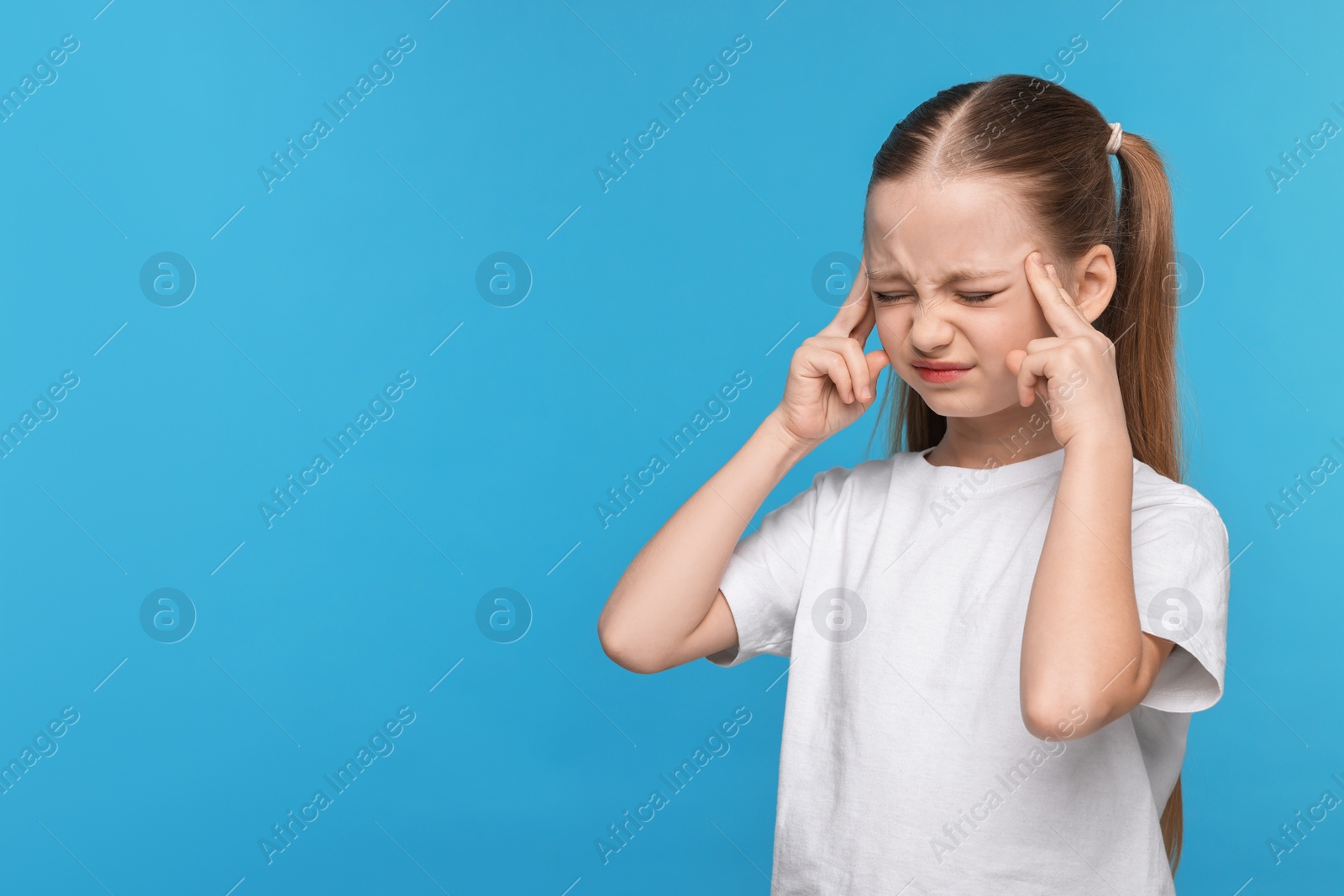 Photo of Little girl suffering from headache on light blue background. Space for text