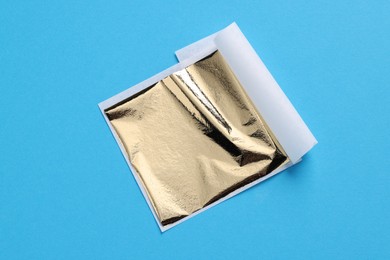 Photo of Edible gold leaf sheet on light blue background, top view