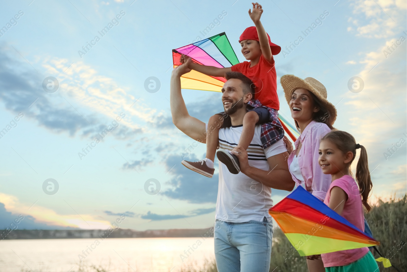 Photo of Happy parents and their children playing with kites outdoors at sunset. Spending time in nature