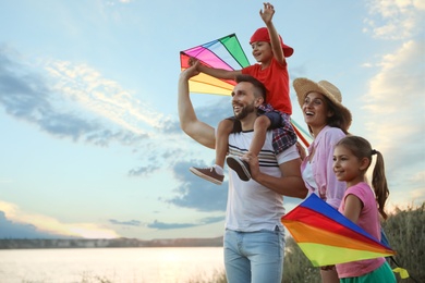 Photo of Happy parents and their children playing with kites outdoors at sunset. Spending time in nature