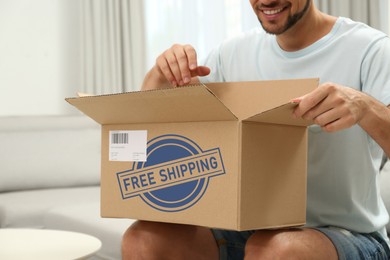 Image of Happy man opening parcel on sofa at home, closeup. Free shipping
