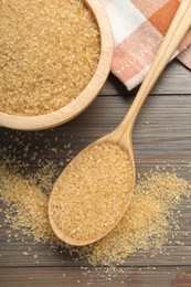 Brown sugar in bowl and spoon on wooden table, flat lay