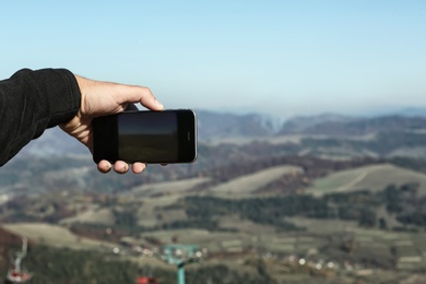 Man taking photo of beautiful mountain landscape with smartphone