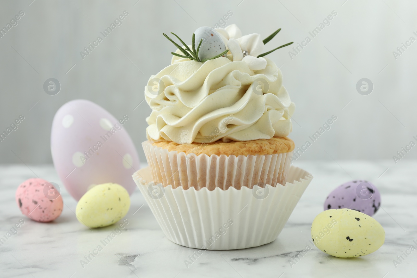 Photo of Tasty Easter cupcake with vanilla cream and candies on white marble table