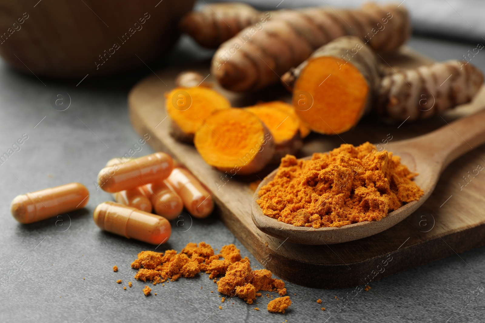 Photo of Aromatic turmeric powder and pills on grey table, closeup. Space for text