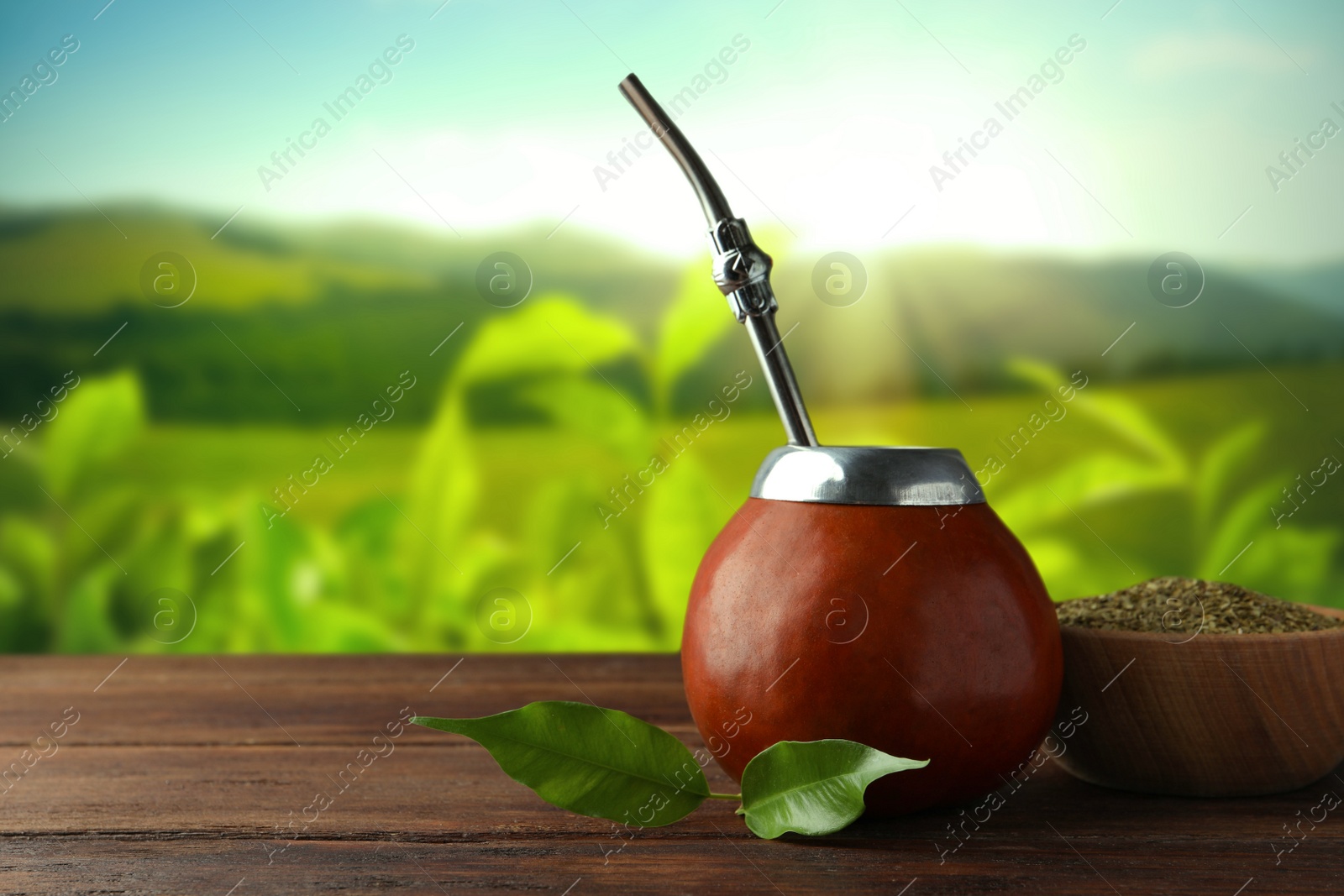 Image of Calabash with mate tea and bombilla on wooden table outdoors. Space for text