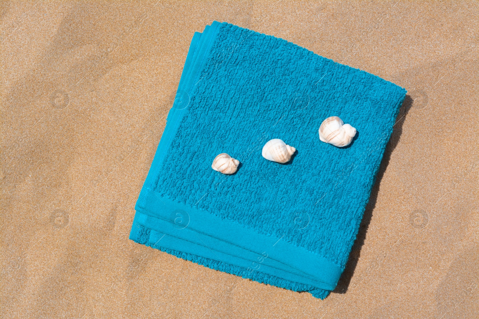 Photo of Folded soft blue beach towel with seashells on sand, flat lay