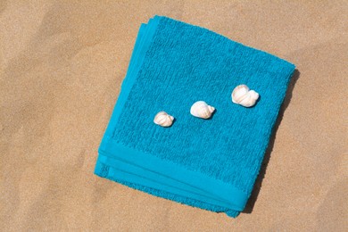 Folded soft blue beach towel with seashells on sand, flat lay