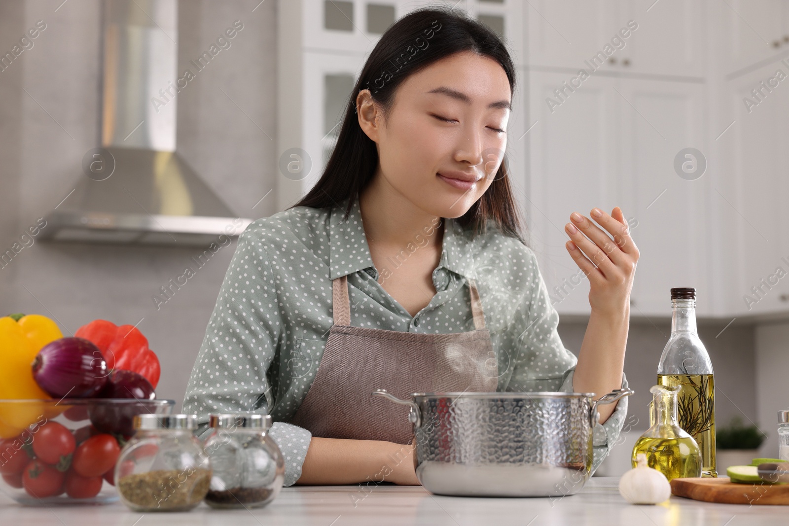 Photo of Beautiful woman smelling soup after cooking at countertop in kitchen