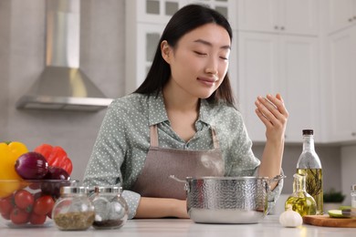 Beautiful woman smelling soup after cooking at countertop in kitchen