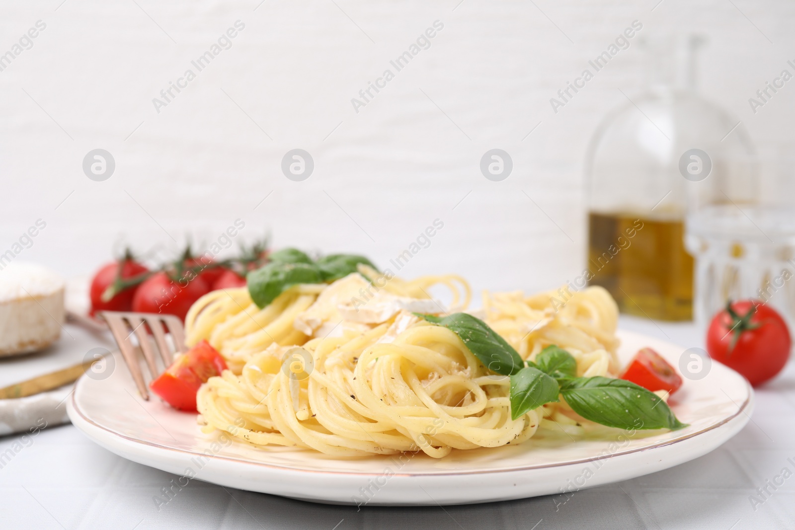 Photo of Delicious pasta with brie cheese, tomatoes and basil leaves on white tiled table, closeup. Space for text